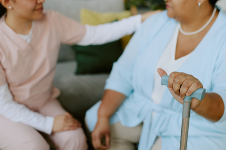 Nurse and senior African American female patient sitting on sofa and having heart to heart talk...