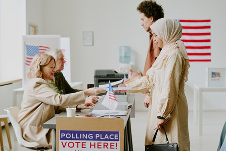 Biracial young man and woman in hijab taking ballot papers at polling station on election day, side view shotの写真素材