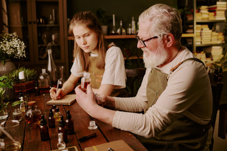 Mature perfumer showing his brand new sample of unique perfume while his granddaughter admiring it...