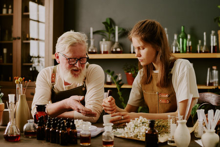 Mature perfumer giving advices to his female student while she listening to him carefully and crushing herbs with help of ceramic mortar and pestleの写真素材