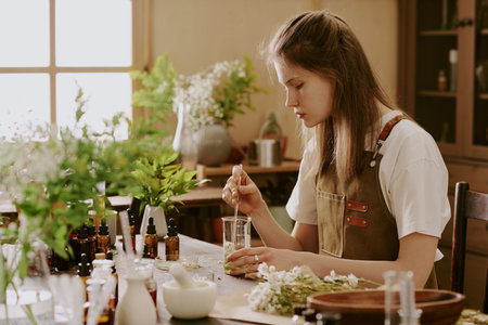 Female young intern mixing dried crushed daisy petals with organic light green liquidの写真素材