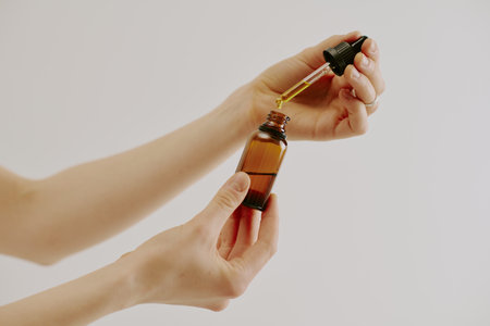 Female hands holding brown glass bottle and glass pipette full of organic golden essenceの写真素材