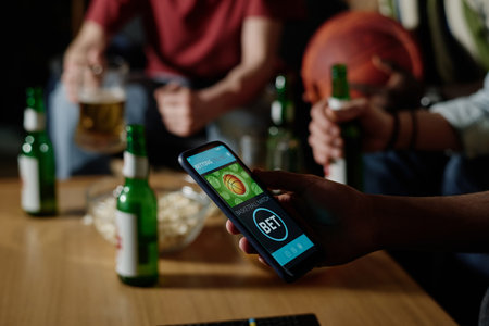 Unrecognizable man holding smartphone betting on favorite team while watching basketball game with his friends in eveningの写真素材