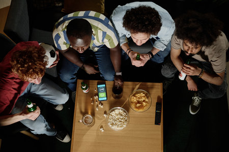 From above view of four ethnically diverse friends sitting in living room watching sports event and...