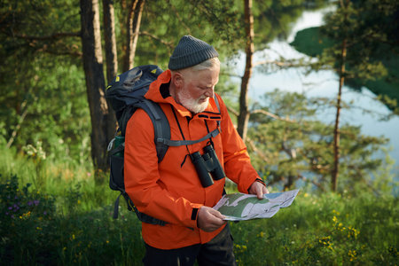 High angle view medium shot of senior Caucasian traveler wearing backpack reading paper mapの写真素材