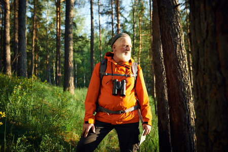 Medium long portrait senior Caucasian tourist wearing orange jacket with beanie standing in mountain...