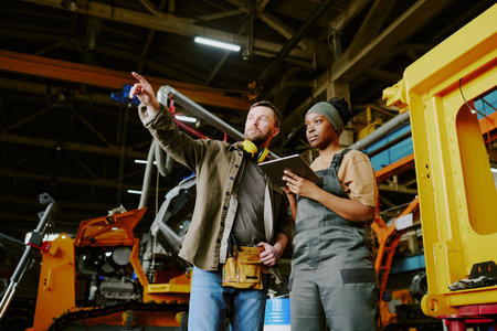 Low angle view of mature Caucasian engineer showing new equipment to his Black female colleague at...