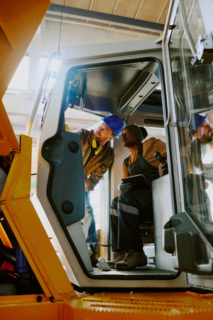 Vertical shot of two ethnically diverse engineers doing quality control of new bulldozer at work in modern factoryの写真素材