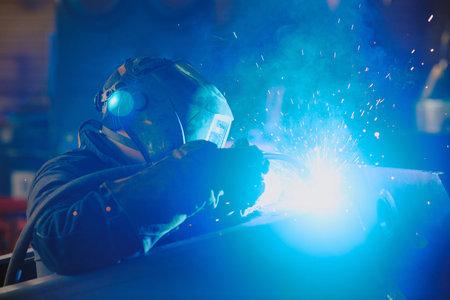 Medium closeup of professional welder in protective clothes and helmet using torch at work, copy spaceの写真素材