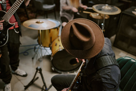 High angle view of unrecognizable man in hat sitting on chair and playing guitar during rehearsal or performance with bandの写真素材