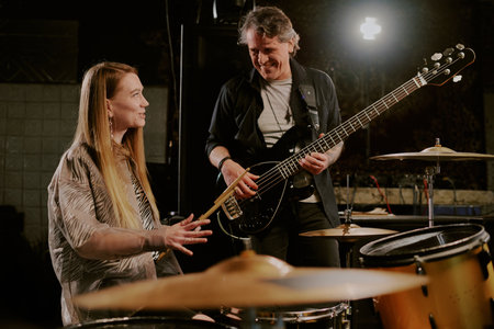 Joyful young female drummer and mature male bassist talking while having rehearsal in garageの写真素材