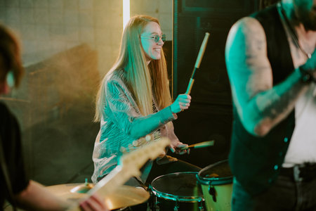 Selective focus shot of young female musician with long blond hair enjoying playing drums in rock bandの写真素材