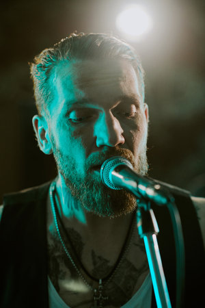 Vertical closeup portrait of bearded gen X rock vocalist singing power ballad during live show