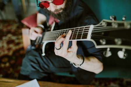 High angle view of bearded rock musician wearing red sunglasses playing electric guitar
