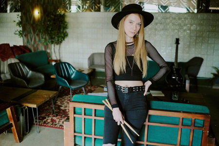 Young Caucasian rock musician holding drumsticks standing relaxed in room in abandoned house looking at cameraの写真素材