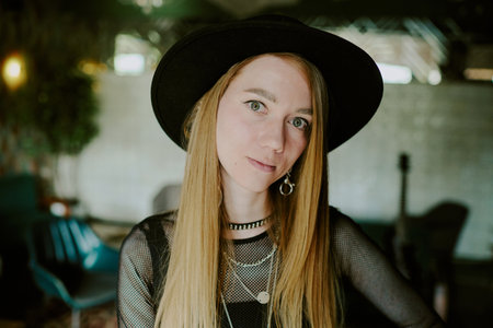 Medium closeup of young Caucasian female rock musician with long hair wearing hat looking at cmaeraの写真素材