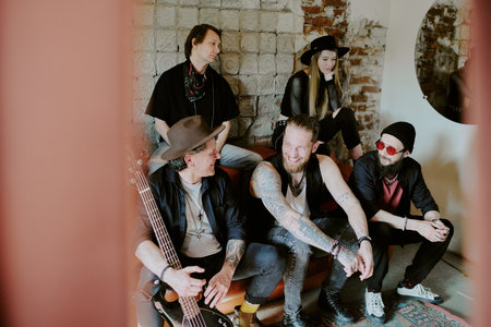 Modern gen X rock band musicians sitting on leather sofa in abandoned building enjoying conversationの写真素材