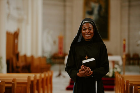 Medium shot of cheerful African American Catholic nun holding Bible book standing at nave, smiling...