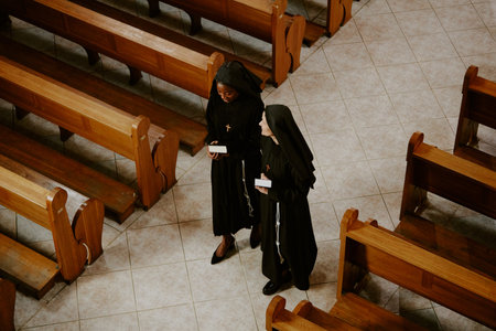 High angle view of two ethnically diverse young and mature Catholic nuns walking along nave and having conversationの写真素材