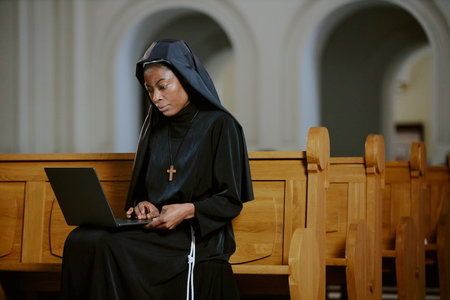 Medium shot of young African American nun sitting on wooden bench in Catholic church working on...