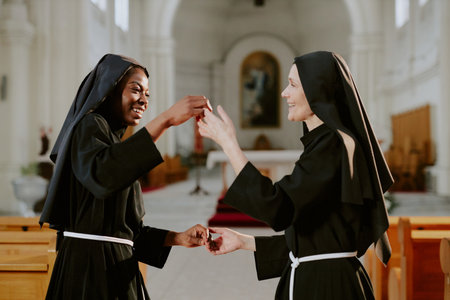 Two ethnically diverse mature and young Catholic nuns enjoying dancing at nave in church, medium shotの写真素材