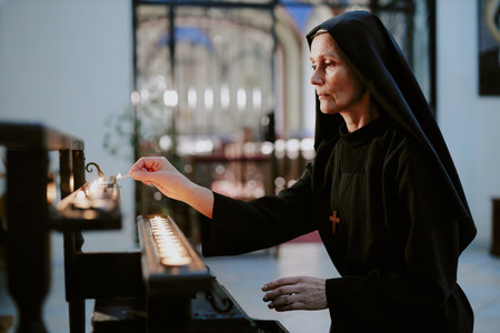 Medium shot of mature Caucasian Catholic nun holding burning match lighting up candles in church, copy spaceの写真素材
