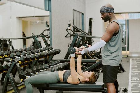 African American coach helping his female client with bulking muscles, they doing bench press togetherの写真素材