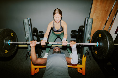 Female athlete helping her shredded African American friend with lifting heavy weight