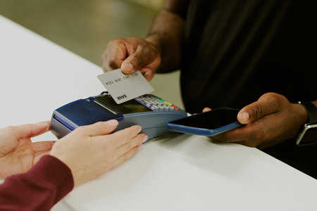African American man making payment using his silver card, female hand holding payment terminal