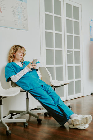 Young blonde Caucasian nurse spending her free time in world wide web while she sitting on plastic chair in on call roomの写真素材