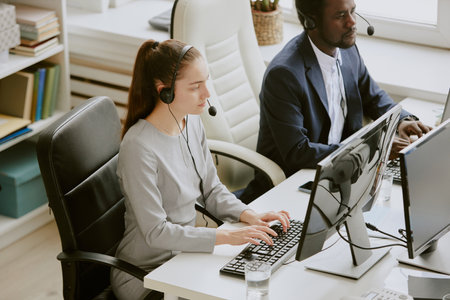 African American and Caucasian call center specialists dressed in business clothes using computers...
