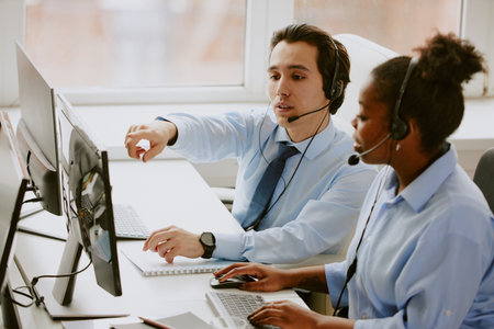 Caucasian male operator helping his African American female colleague with application launched on...