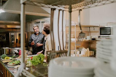 Two highly skilled cooks standing in center of restaurant kitchen and discussing cooking process of famous dishの写真素材