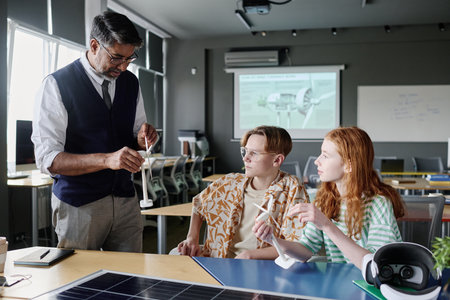 Medium long shot of mature teacher of Environmental Education showing teen students modern wind...