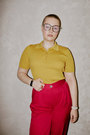 Vertical medium long shot of confident Caucasian woman with buzz cut wearing yellow top and red pants posing for cameraの写真素材