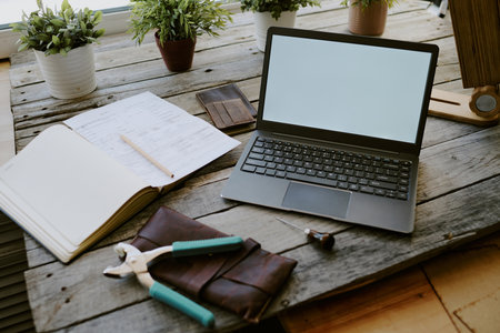 Black laptop surrounded by notes and leather goods on gray wooden table, four clay pots with plants in backgroundの写真素材