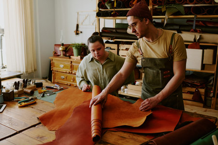 Caucasian male tailor rolling leather roll up to show it to his female client with down syndromeの写真素材