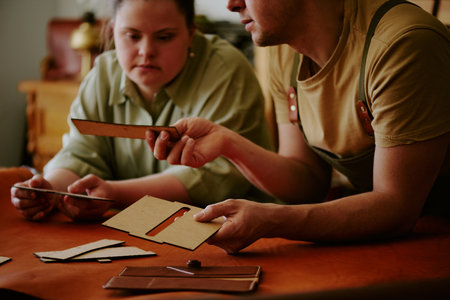 Male tailor demonstrating wooden rectangular shape to his female coworker with down syndrome while...