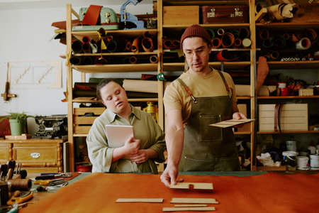Male tailor choosing wooden shape to create leather good while his female assistant with down...