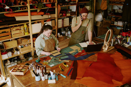 Female tailor with down syndrome cutting out workpieces while her male colleague taking orders via...