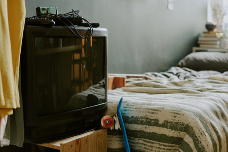 Medium close up of retro TV with console on top, single bed covered with striped linenの写真素材