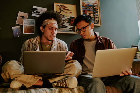 Biracial programmers sitting on bed while discussing technical problems and trying to solve them...