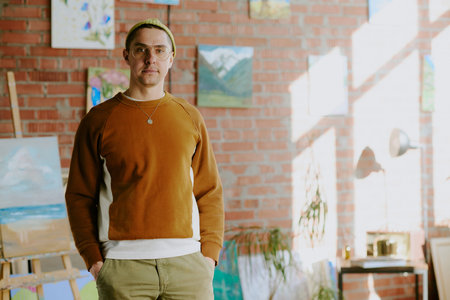 Medium portrait of young Caucasian man wearing casual clothes standing with hands in pockets in his art studio, copy spaceの写真素材