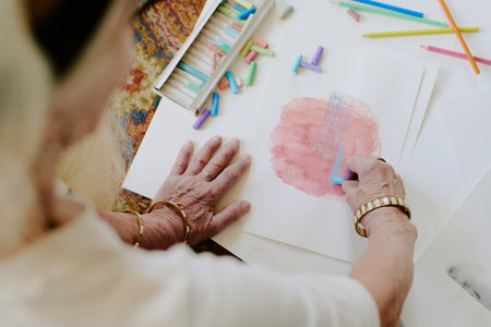 High angle view of unrecognizable senior woman sitting on floor and drawing colorful picture with pastelsの写真素材