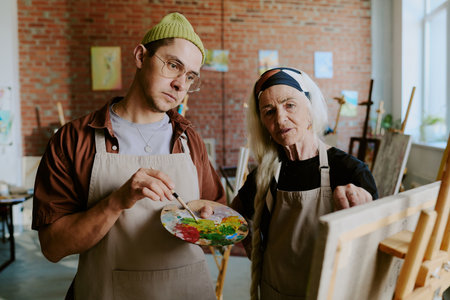 Senior Caucasian woman teaching young man how to paint picture on canvas during individual art class, medium shotの写真素材