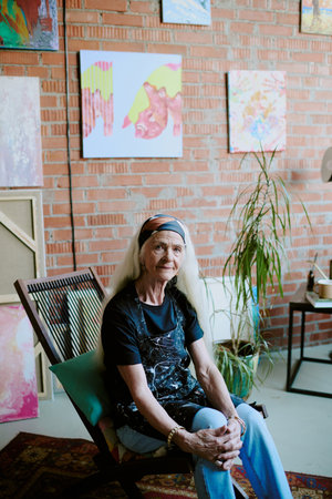 Vertical shot of senior Caucasian woman wearing casual clothes with apron sitting on wooden chair in...