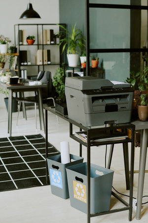 Vertical no people shot of printer on table and recycling bins on floor under it in modern...