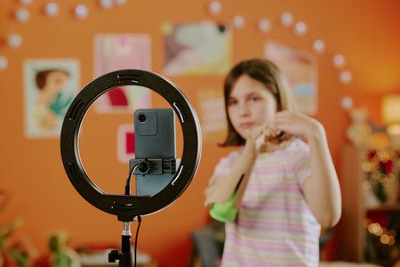 Selective focus of teen girl with arm prosthesis posing while smartphone camera on tripod with LED...
