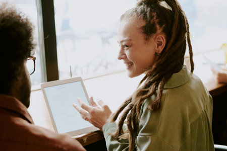 Two people interacting while using tablet in cozy cafe environment with relaxed atmosphere visible....