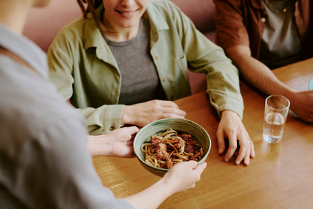 Person providing a bowl of Asian noodles to two people seated at table. Simple and cozy setup with clear focus on the foodの写真素材